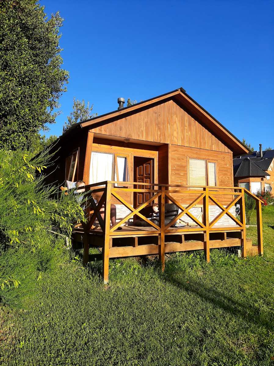 La cabaña de madera entera, con su deck y la baranda, bajo un cielo limpio