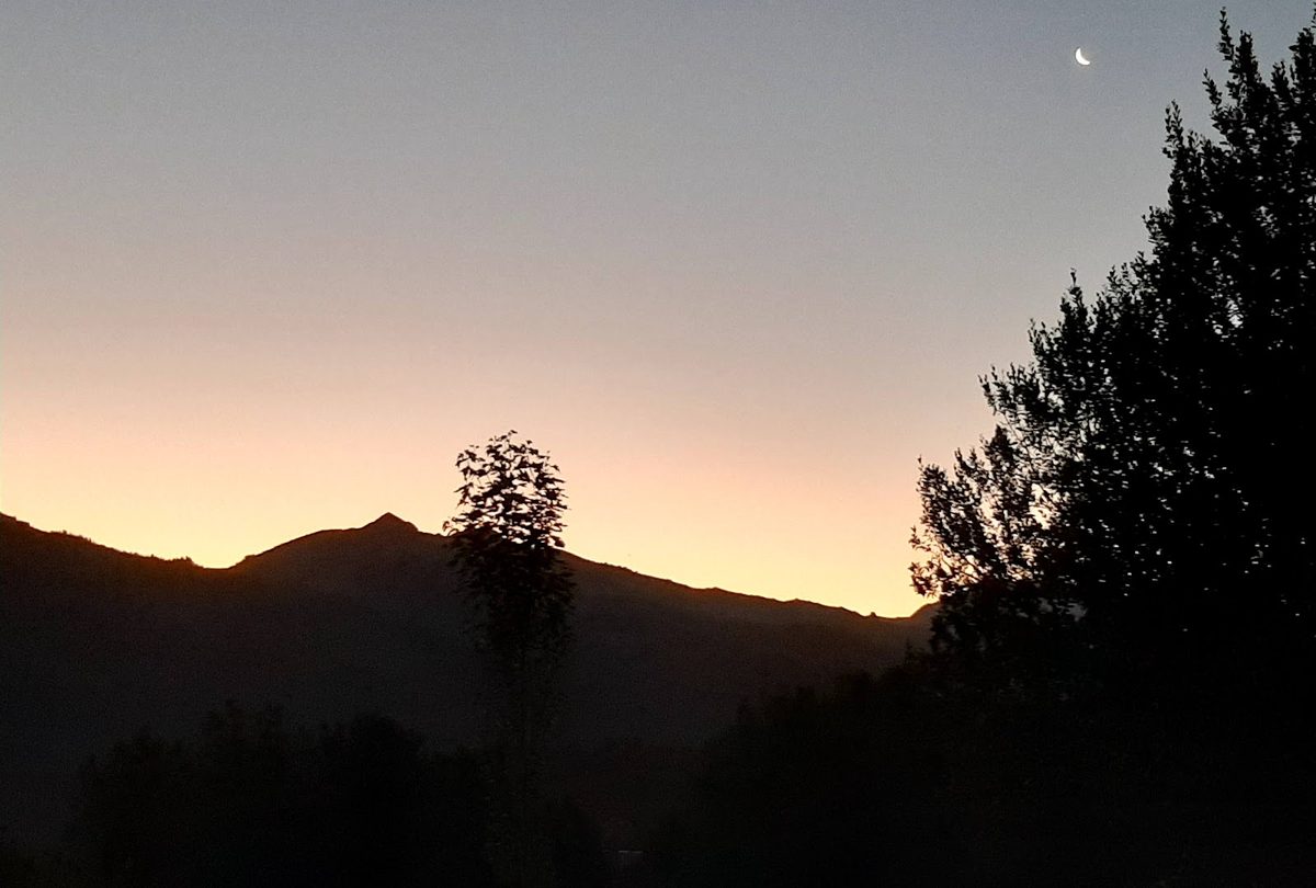 El atardecer con la luna sobre la silueta de la montaña